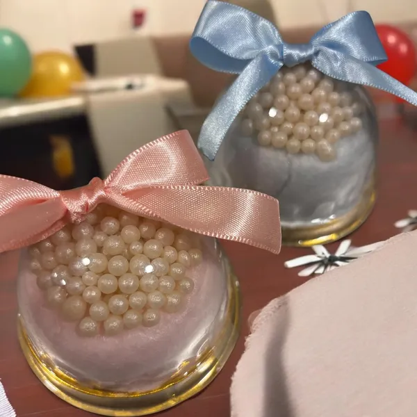 Dois mini-cakes de algodão-doce rosa e azul em embalagens transparentes, com laços e decoração de pérolas