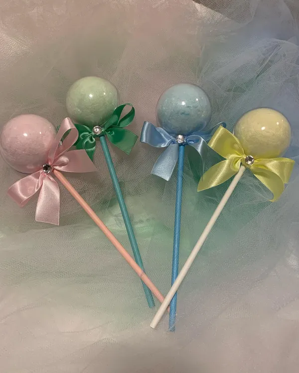Quatro pirulitos em esfera acrílica com laços rosa, verde, azul e amarelo